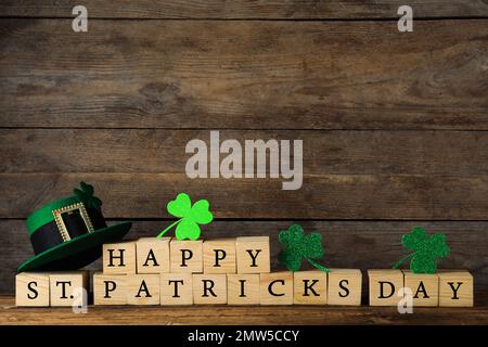 Holzwürfel mit Wörtern HAPPY St. PATRICK's DAY, grüner Koboldhut und Kleeblätter auf dem Tisch Stockfoto