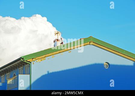 Ein Fragment der Fassade eines blauen Hauses am Hintergrund des Himmels mit einer großen Zirruswolke Stockfoto