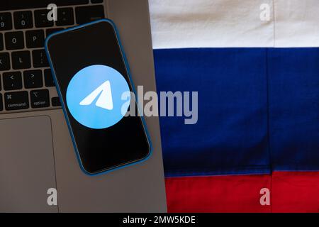 In dieser Fotoabbildung wird ein Telegramm Messenger App Logo auf dem Bildschirm eines Mobiltelefons mit einem Hintergrund aus Laptop-Tastatur und russischer Flagge angezeigt. Stockfoto