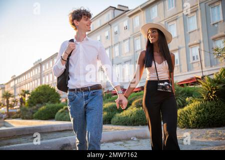 Ein multiethnisches Paar im Urlaub, das Händchen hält und im Stadtzentrum spaziert Stockfoto