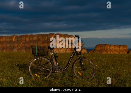 Heubälle und Elektrofahrrad auf dem Feld bei Ceske Budejovice Stadt in Sonnenaufgang Zeit in Farbe Herbst Stockfoto