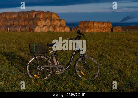 Heubälle und Elektrofahrrad auf dem Feld bei Ceske Budejovice Stadt in Sonnenaufgang Zeit in Farbe Herbst Stockfoto