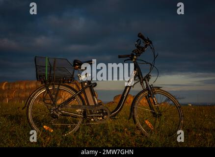 Heubälle und Elektrofahrrad auf dem Feld bei Ceske Budejovice Stadt in Sonnenaufgang Zeit in Farbe Herbst Stockfoto