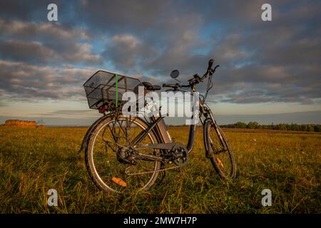 Heubälle und Elektrofahrrad auf dem Feld bei Ceske Budejovice Stadt in Sonnenaufgang Zeit in Farbe Herbst Stockfoto