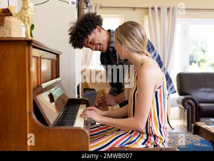 Glückliches, vielseitiges Paar, das zu Hause viel Spaß beim Klavierspielen hat Stockfoto
