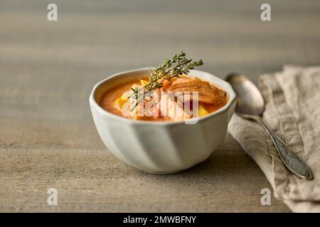 Schale mit hausgemachtem Lachs und Tomatensuppe auf einem Holzküchentisch Stockfoto