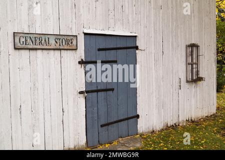 Alte, weiß lackierte Holzfassade mit vertikaler Holzdiele, dunkelgraue Eingangstür und General Store-Schild im Herbst. Stockfoto