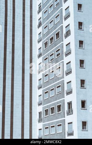 Vertikale Aufnahme eines hohen Wohngebäudes mit Schwerpunkt auf einer Fassade mit horizontalen Details in dunkelgrauer Farbe, die sich von dieser unterscheidet Stockfoto