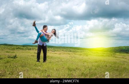 Ein glückliches Paar, das auf dem Feld verliebt ist, ein glücklicher Mann, der seine Freundin auf dem Feld trägt Stockfoto