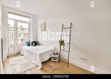 Ein Schlafzimmer mit weißen Wänden und Hartholzfußboden im Zimmer, es gibt eine Leiter an der Wand Stockfoto