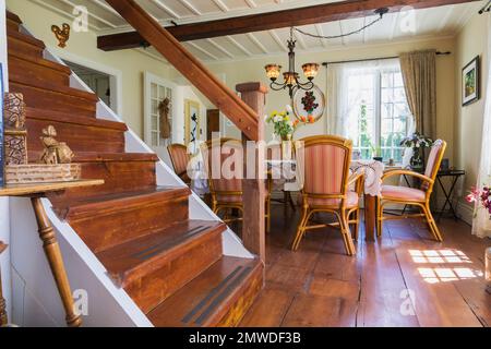 Holztreppe führt in die obere Etage und Esszimmer mit Rattansesseln und Holztisch in einem alten rekonstruierten Haus im kanadianischen Stil aus dem Jahr 1886. Stockfoto