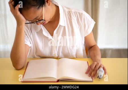 Junge asiatische Frauen sitzen allein in ihrem Zimmer und weinen mit dem Gesicht nach unten, während sie das leere Buch auf den Schreibtisch legen. Einsamkeit, Stress und Angst. Stockfoto