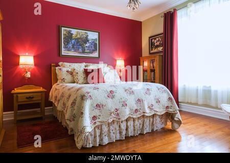 Queen-Size-Bett mit Nachttisch aus Eichenholz und Glasschrank im Hauptschlafzimmer im Erdgeschoss in einem zeitgenössischen Landhausstil. Stockfoto