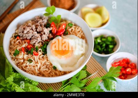 Nudelschüssel mit gekochtem Ei Hackfleisch Schweinefleisch Gemüse Frühlingszwiebeln Zitrone Limette Salat Sellerie und Chili auf dem Tisch Essen, Instantnudeln kochen leckeres Essen Stockfoto