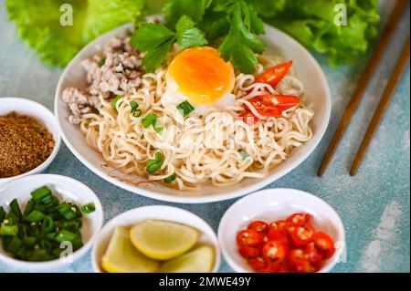 Nudelteller mit Eierhackfleisch, Gemüse, Frühlingszwiebeln, Zitronensalat, Sellerie und Chili auf dem Tisch, Instant-Nudeln, die köstlich kochen Stockfoto