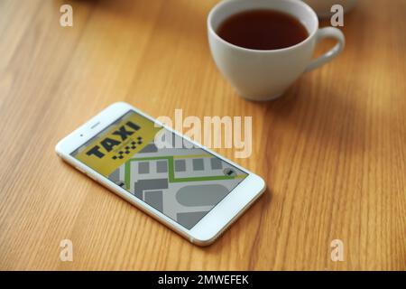 Smartphone mit Taxianwendung und Tasse Tee auf Holztisch Stockfoto