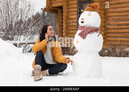 Junge Frau in der Nähe von witzigen Schneemännern im Freien. Winterurlaub Stockfoto