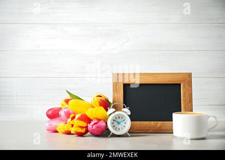 Tafel mit Morgenwunsch, köstlichem Kaffee, Tulpen und Wecker auf hellgrauem Tisch Stockfoto