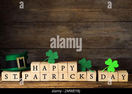 Holzwürfel mit Wörtern HAPPY St. PATRICK's DAY, grüner Koboldhut und Kleeblätter auf dem Tisch Stockfoto