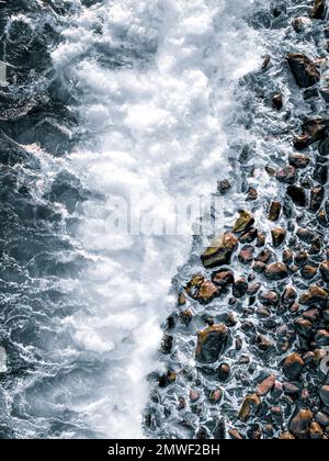 Ein vertikales Bild von einem felsigen Strand mit Wellen, die die Küste spülen Stockfoto