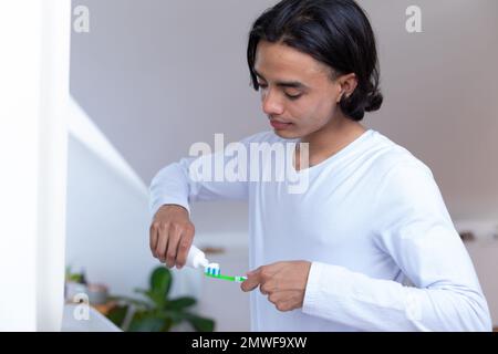 Ein glücklicher birassistischer Mann, der im Badezimmer Zähne putzt Stockfoto