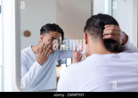 Ein glücklicher birassistischer Mann, der im Badezimmer in den Spiegel schaut Stockfoto