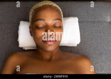 Glückliche afroamerikanische Frau, die mit geschlossenen Augen auf einem Handtuch lag Stockfoto