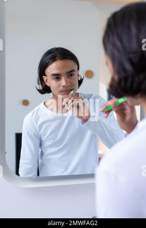 Ein glücklicher birassistischer Mann, der im Badezimmer Zähne putzt Stockfoto