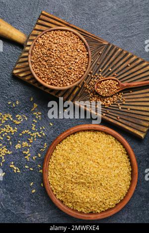 Schalen mit Buchweizen und Bulgur auf dunklem Hintergrund Stockfoto