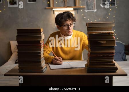Frustrierter Student, der am späten Abend oder Abend vor der Prüfung studiert, Schüler mit einem Haufen Bücher, der hart für die Prüfung in der Highschool lernt. Kopie SPA Stockfoto