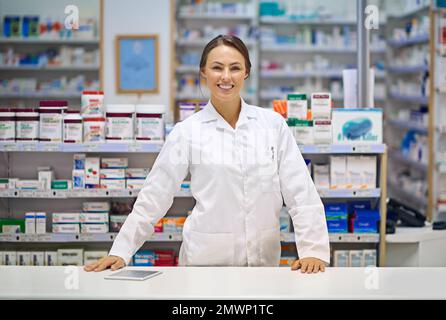 Ihr freundlicher und erfahrener lokaler Apotheker. Porträt eines attraktiven jungen Apothekers, der an der Rezepttheke steht. Stockfoto