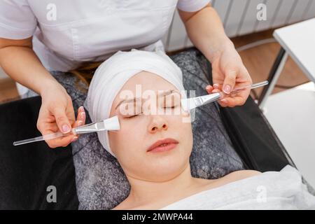 Kosmetikerin mit Ton Gesichtsmaske auf Frau Gesicht. Kosmetikerarbeit Stockfoto