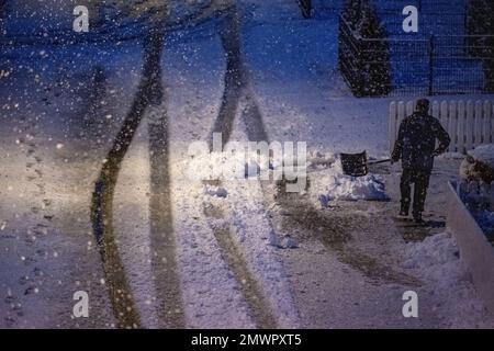 Straubing, Deutschland. 02. Februar 2023. Am frühen Morgen läuft ein Mann mit einer Schneeschaufel auf einer schneebedeckten Straße. Kredit: Armin Weigel/dpa/Alamy Live News Stockfoto