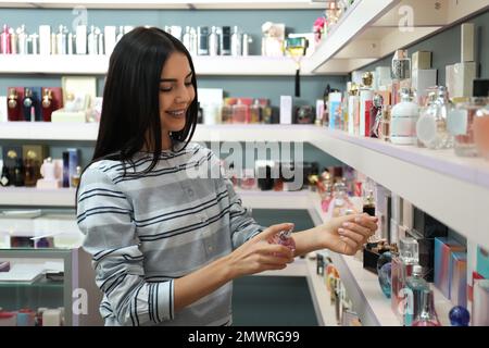 Junge Frau, die Parfüm in einem modernen Laden aufbringt Stockfoto