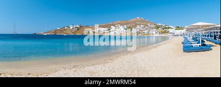 Mykonos Strand im Sommer mit Sonnenschirm und luxuriösen Liegestühlen, blauer Ozean mit dem Berg am Elia Beach Mikonos Griechenland. Stockfoto