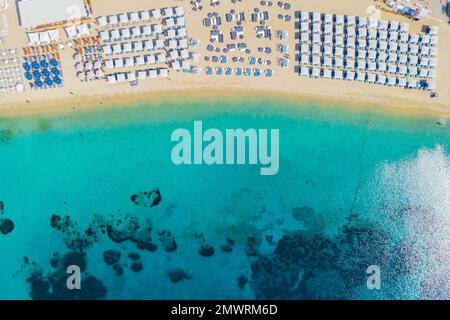 Mykonos Strand im Sommer mit Sonnenschirm und luxuriösen Liegestühlen, blauer Ozean mit dem Berg am Elia Beach Mikonos Griechenland. Stockfoto