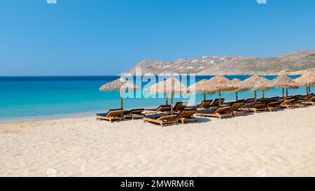 Mykonos Strand im Sommer mit Sonnenschirm und luxuriösen Liegestühlen, blauer Ozean mit dem Berg am Elia Beach Mikonos Griechenland. Stockfoto