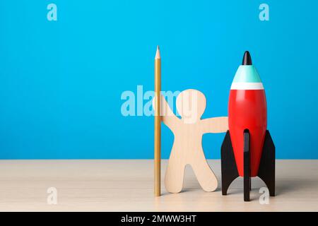 Helle Spielzeugrakete, menschliches Modell und Bleistift auf weißem Holzschreibtisch. Platz für Text Stockfoto