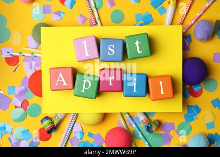 Bunte Würfel mit den Worten 1. APRIL auf gelbem Hintergrund, flach liegend Stockfoto