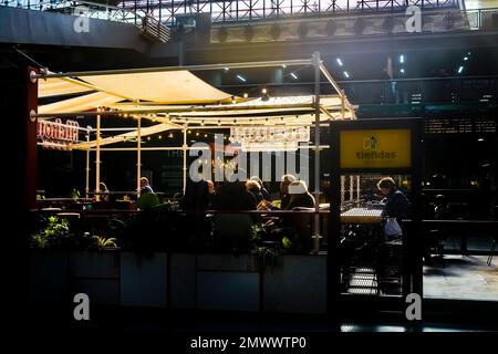 Ein Silhouettenblick von Menschen, die in einem Café im Bahnhof Atocha sitzen, mit hellem Oberlicht im Hintergrund. Stockfoto