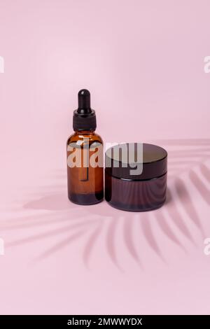 Set mit Hautpflegeprodukten auf brauner Glasverpackung auf pinkfarbenem Hintergrund. Gesichts- und Körperbehandlungskonzept. Natürliche Kosmetik, Modell mit Palmen Stockfoto
