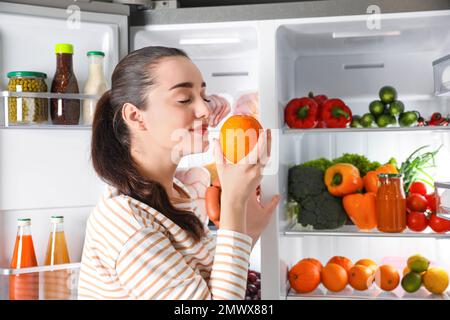 Junge Frau mit orangefarbenem Kühlschrank im Haus Stockfoto