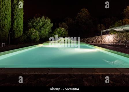 Beleuchteter Swimmingpool auf dem Hügel von Montemassi, umgeben von Zypressen und Oleandern in der Provinz Grosseto. Italien Stockfoto