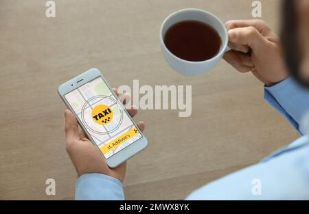 Mann, der Taxi mit Smartphone am Holztisch bestellt, Nahaufnahme Stockfoto