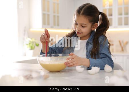 Süßes kleines Mädchen, das Teig am Tisch in der Küche kocht Stockfoto