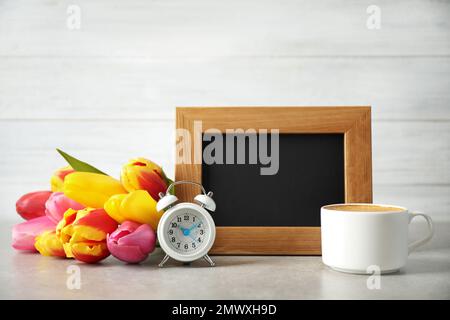 Tafel mit Morgenwunsch, köstlichem Kaffee, Tulpen und Wecker auf hellgrauem Tisch Stockfoto