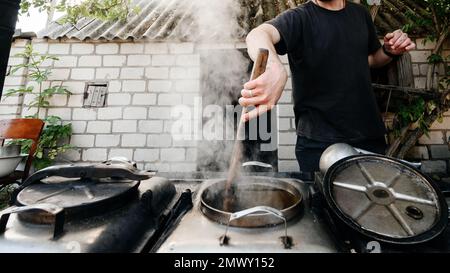 Ein Mann bereitet das Mittagessen in einer Militärküche zu, einem großen Holzspachtel zum Rühren von Essen. Stockfoto