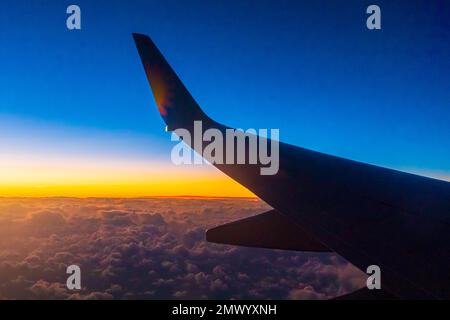 Blick aus dem Passagierfenster eines Boeing 737-Flugzeugs, das über die Wolken bei Sonnenuntergang fliegt Stockfoto