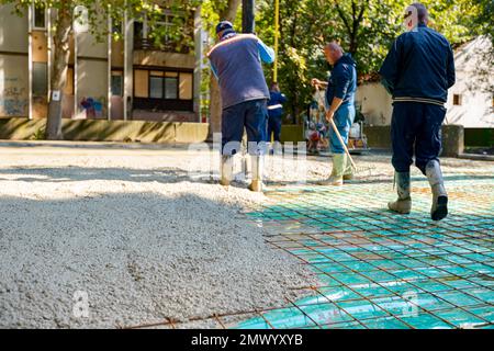 Der Bauarbeiter richtet das Pumpenrohr in die richtige Richtung und gießt eine Betonschicht in das Fundament des Gebäudes. Stützen, Arbeiter verwenden Rechen t Stockfoto