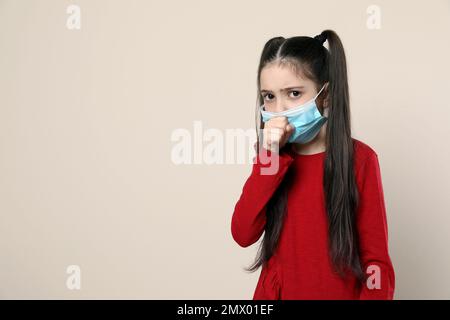 Kleines Mädchen mit medizinischer Maske auf beigefarbenem Hintergrund, Platz für Text. Virenschutz Stockfoto